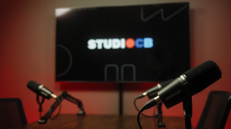 Vista lateral da mesa de podcast mostrando o espaço confortável entre os participantes e a disposição dos microfones.