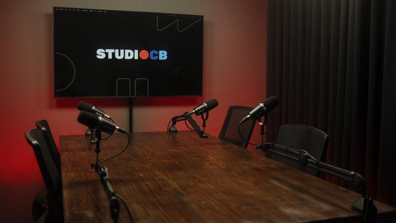 Foto grande angular do estúdio de podcast mostrando o espaço amplo da sala e a disposição da mesa de gravação.