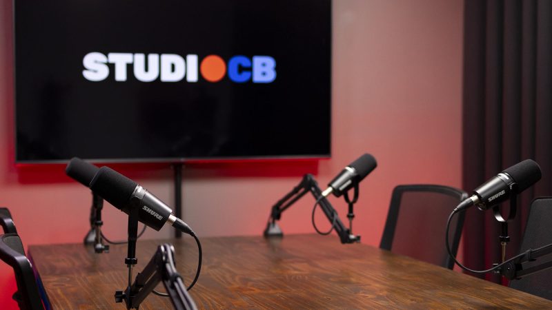 Vista lateral da mesa de podcast mostrando o espaço confortável entre os participantes e a disposição dos microfones.