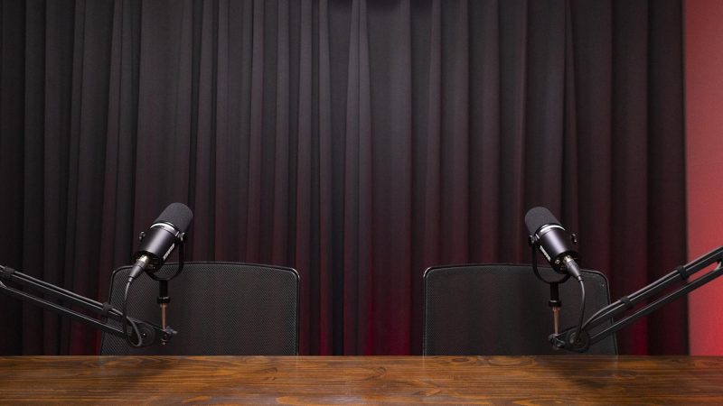 Cenário minimalista com tratamento acústico profissional. Cortinas e revestimentos que garantem som seco e limpo, padrão broadcast.