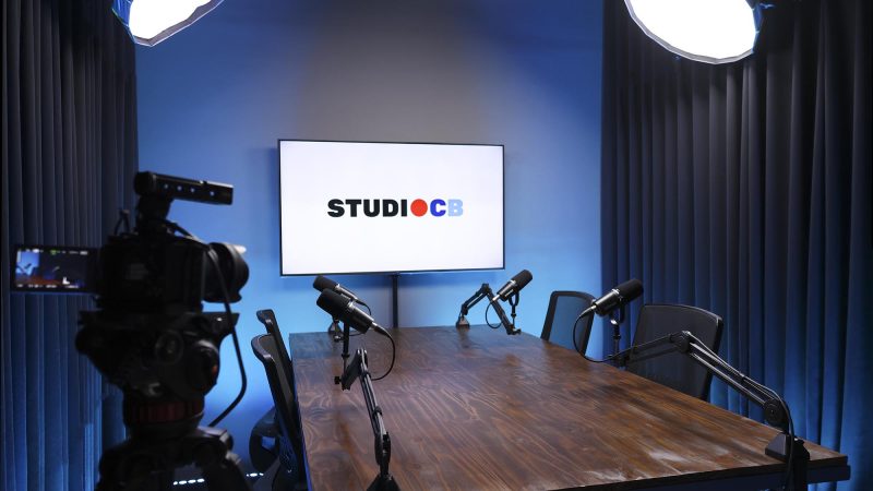 Mesa de podcast ampla com 4 microfones Shure em braços articulados. Ergonomia e qualidade sonora para gravações longas.